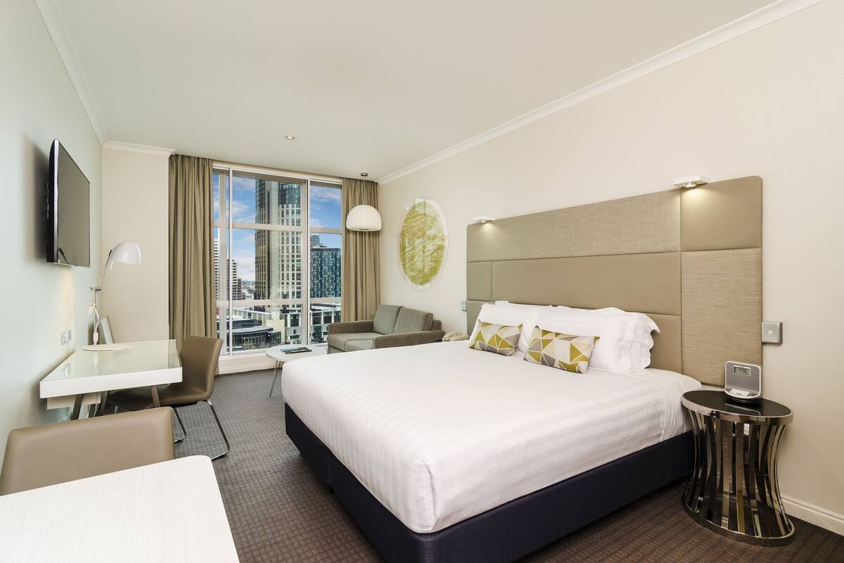 Une chambre d’hôtel avec un grand lit, un bureau, une chaise, une télévision et une vue sur la ville.