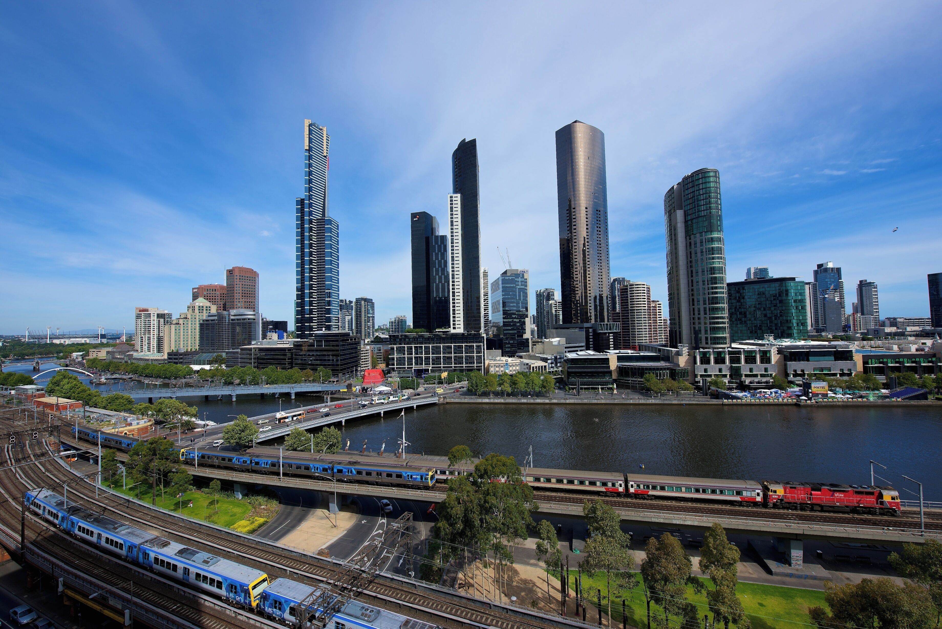 A cityscape with modern skyscrapers, a river, and a train passing by.