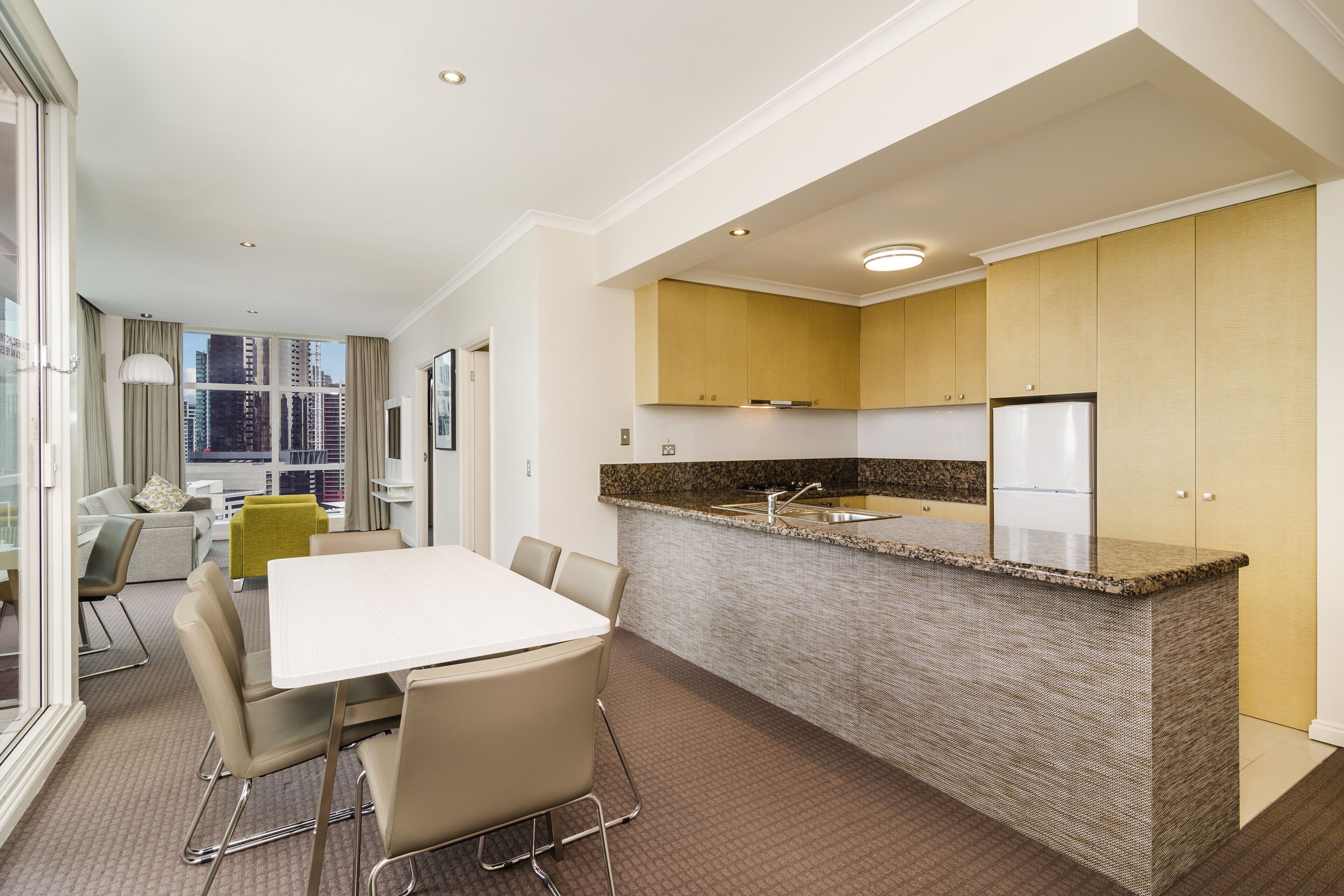 A modern kitchen with a granite countertop, stainless steel appliances, and a dining area with a white table and chairs.