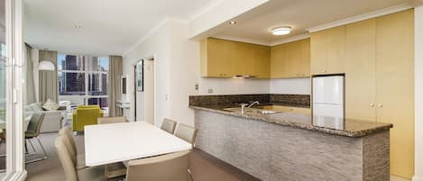 Una cocina moderna con encimera de granito, electrodomésticos de acero inoxidable y una zona de comedor con mesa y sillas blancas.