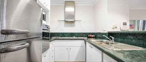 A modern kitchen with stainless steel appliances, white cabinets, and a green marble countertop.