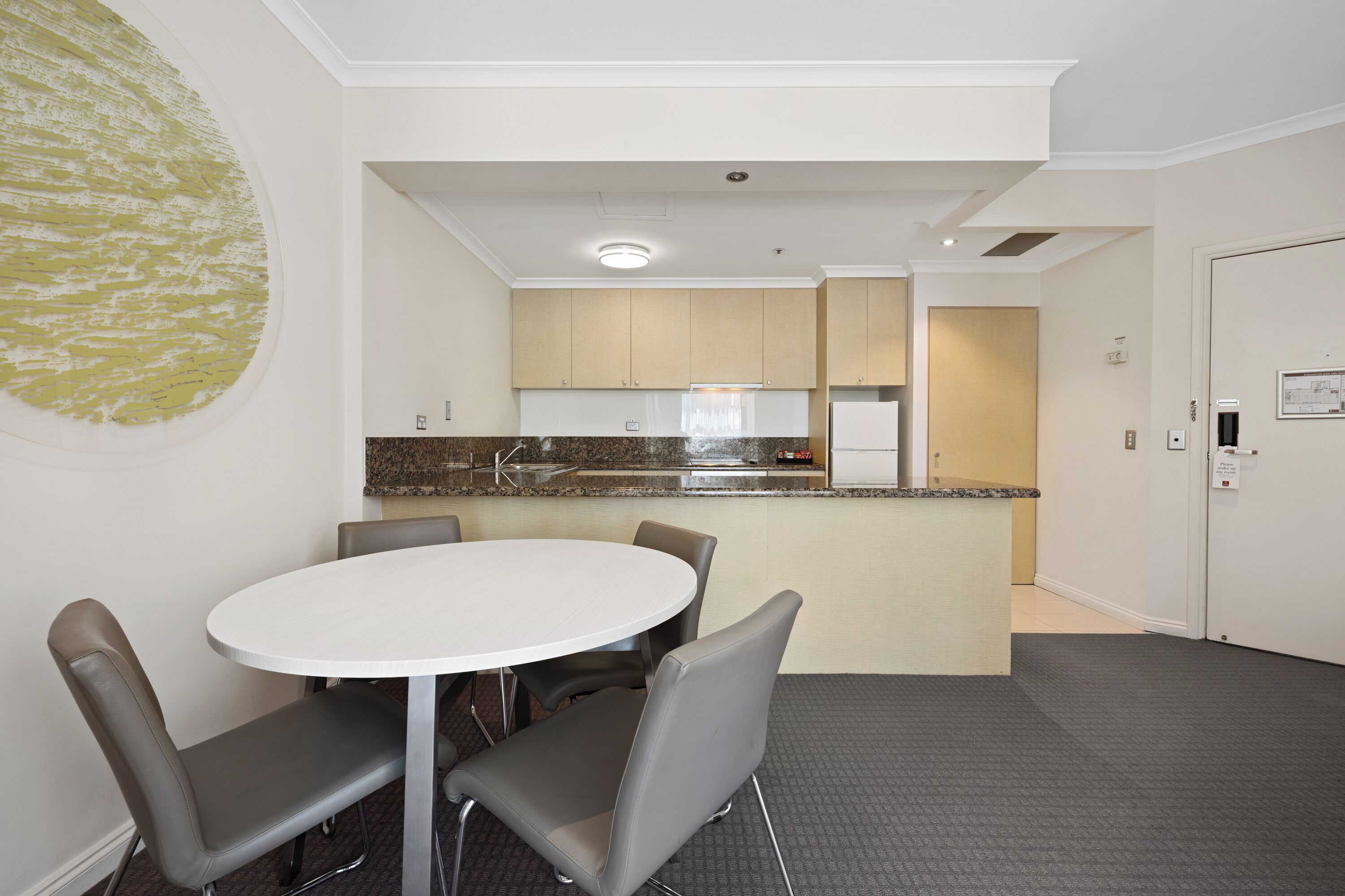 A modern kitchen with a central island, a dining area with a round table and chairs, and a door leading to another room.