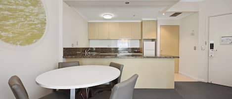 A modern kitchen with a central island, a dining area with a round table and chairs, and a door leading to another room.