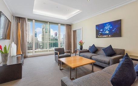 A modern hotel room with a large window offering a city view, a sofa set, a wooden coffee table, and a painting on the wall.