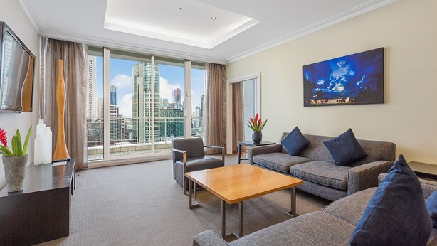 Une chambre d’hôtel moderne dotée d’une grande fenêtre donnant sur la ville, d’un ensemble de canapés, d’une table basse en bois et d’un tableau accroché au mur.