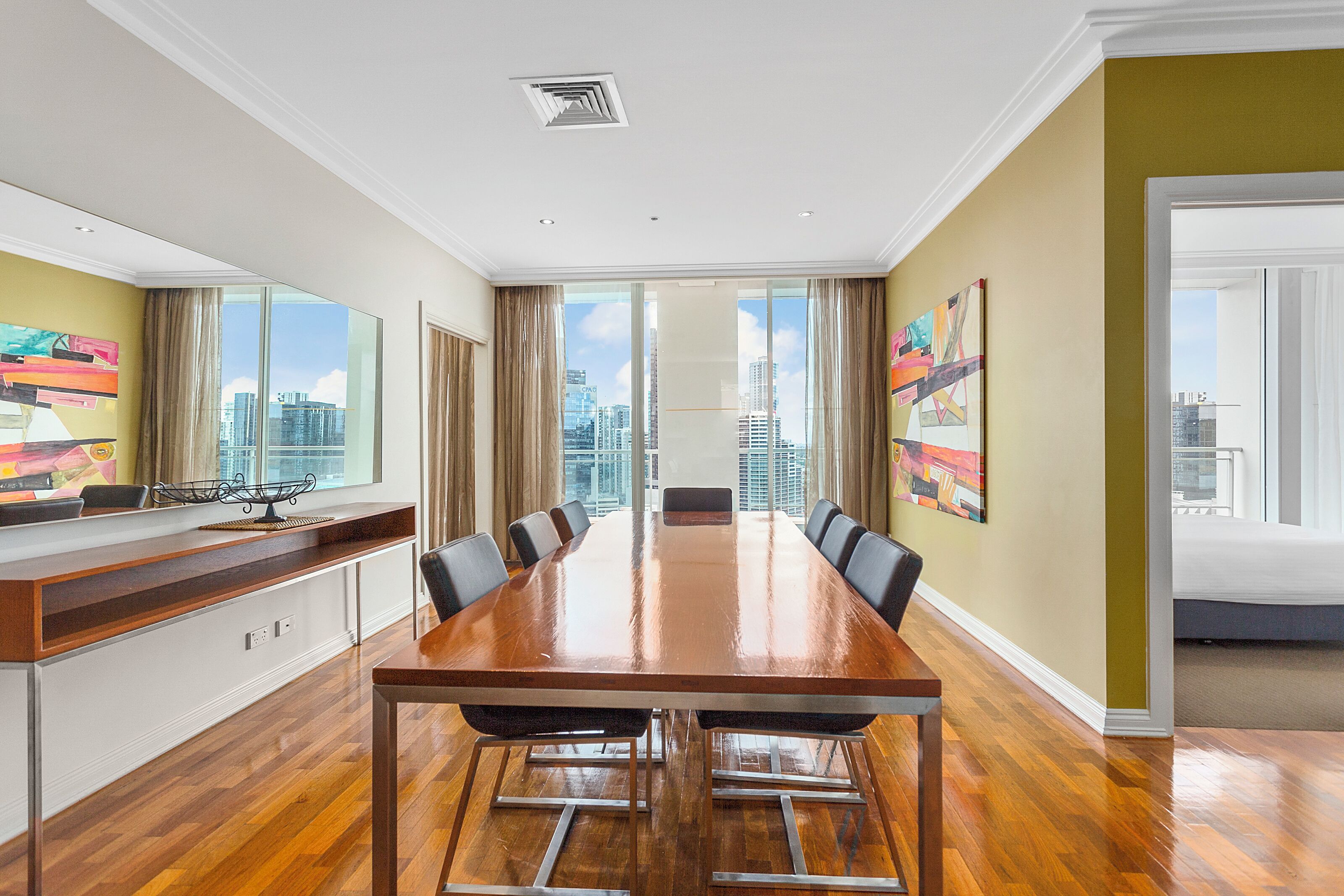 A conference room with a long table, chairs, and a city view through large windows.