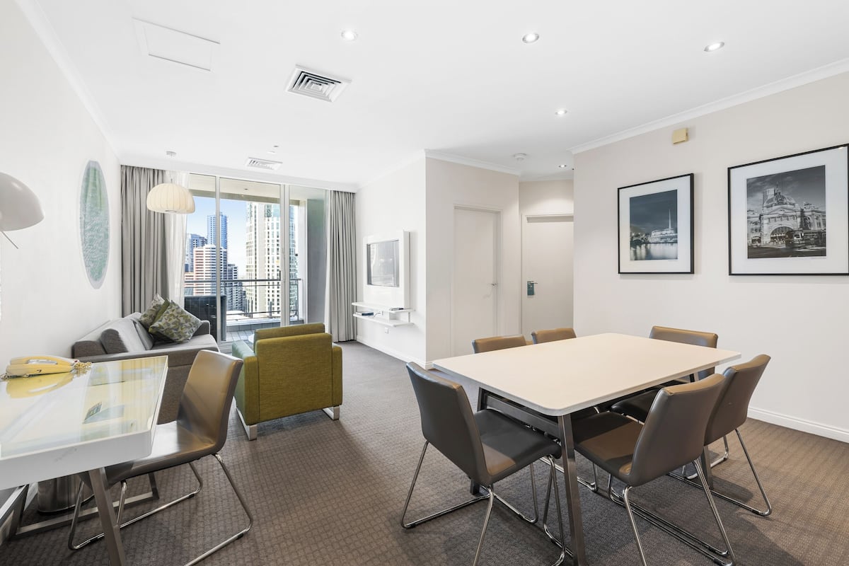Une salle de conférence moderne avec une table en verre, des chaises marron, un canapé jaune et une vue sur la ville.