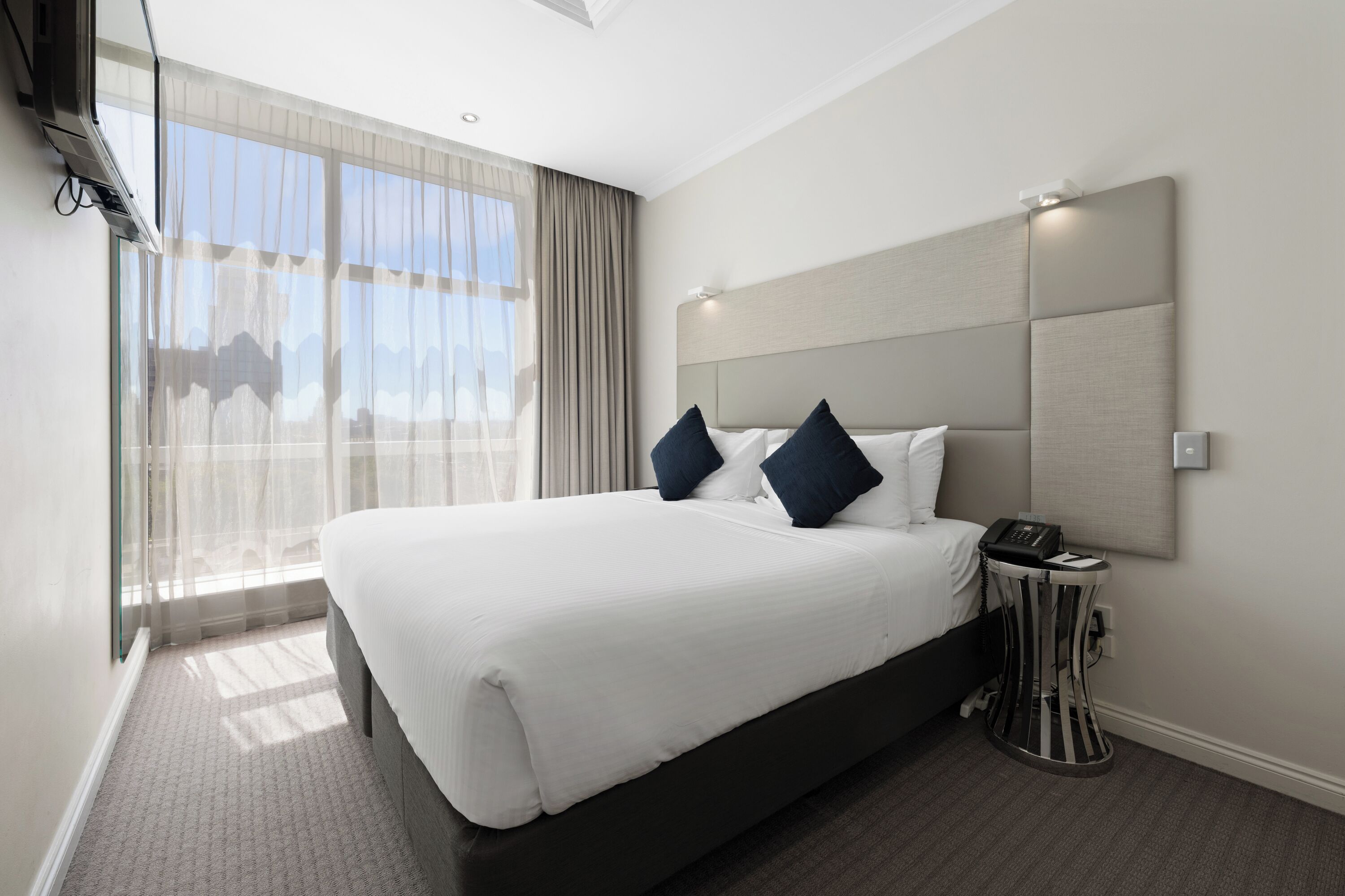 Ein Hotelzimmer mit einem großen Bett, einem Nachttisch mit Telefon und einem Fenster mit Vorhängen.