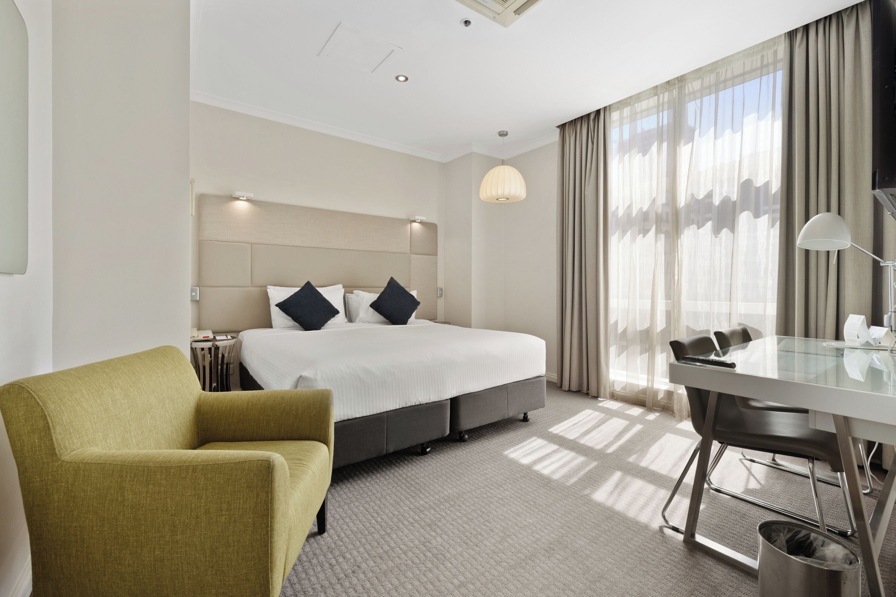 A hotel room with a bed, a desk, a chair, and a lamp.
