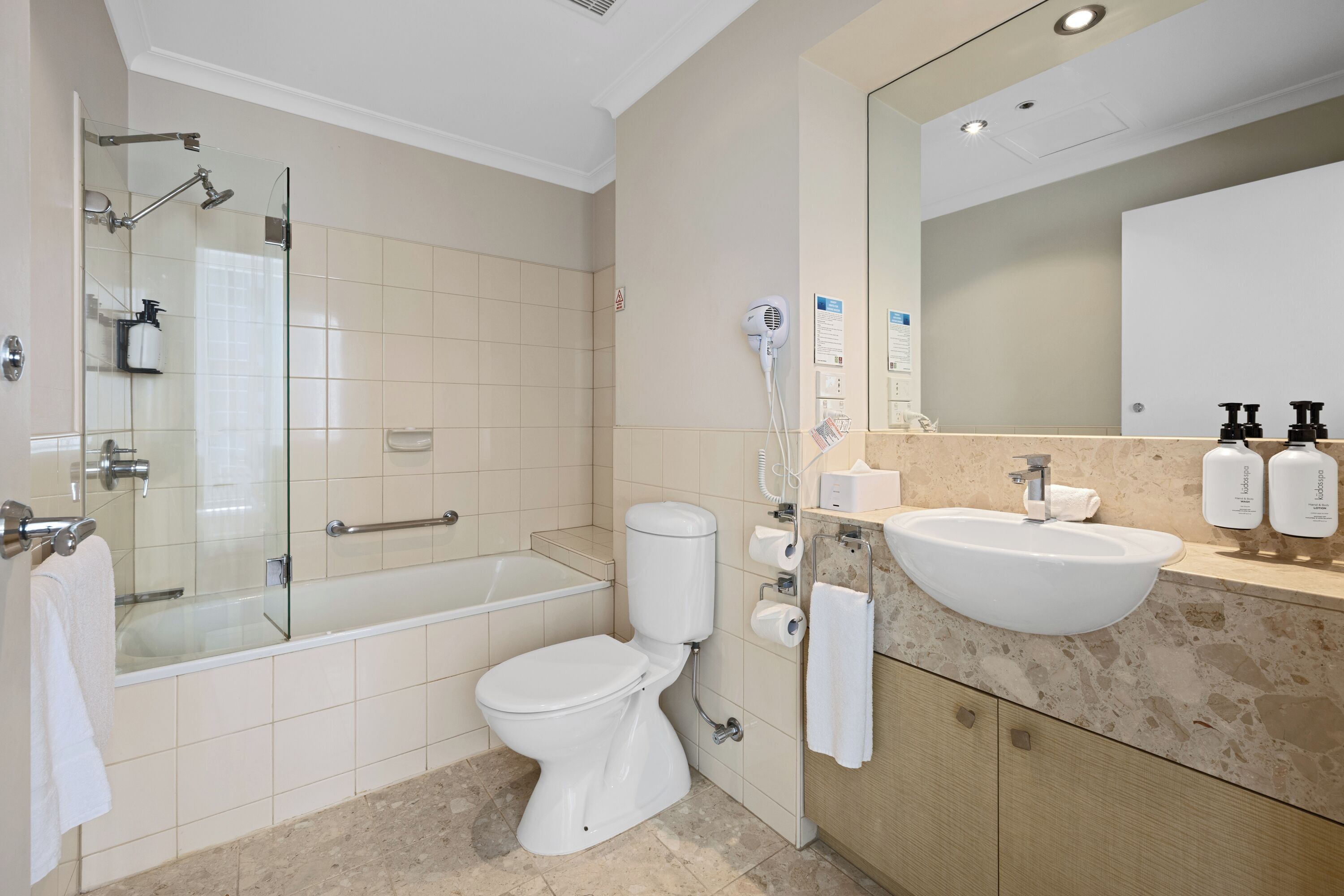 Ein modernes Badezimmer mit einer gläsernen Dusche, einer weißen Toilette, einem Waschbecken mit Marmorplatte und einem großen Spiegel.