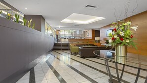Un hall d'entrée moderne avec un comptoir d'accueil en verre, un escalier et un espace salon.