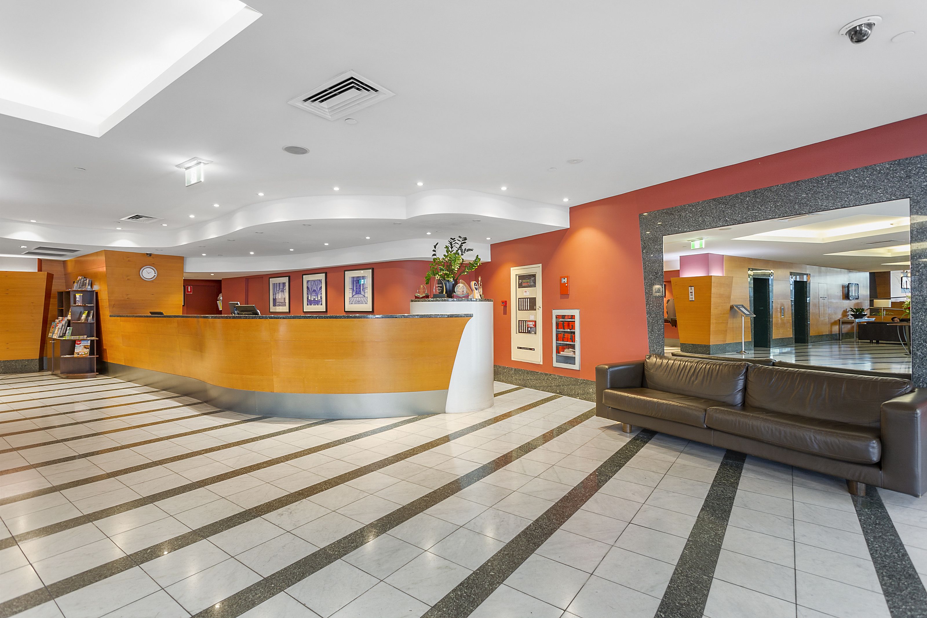 A hotel lobby with a reception desk, a seating area, and a large mirror reflecting the interior.