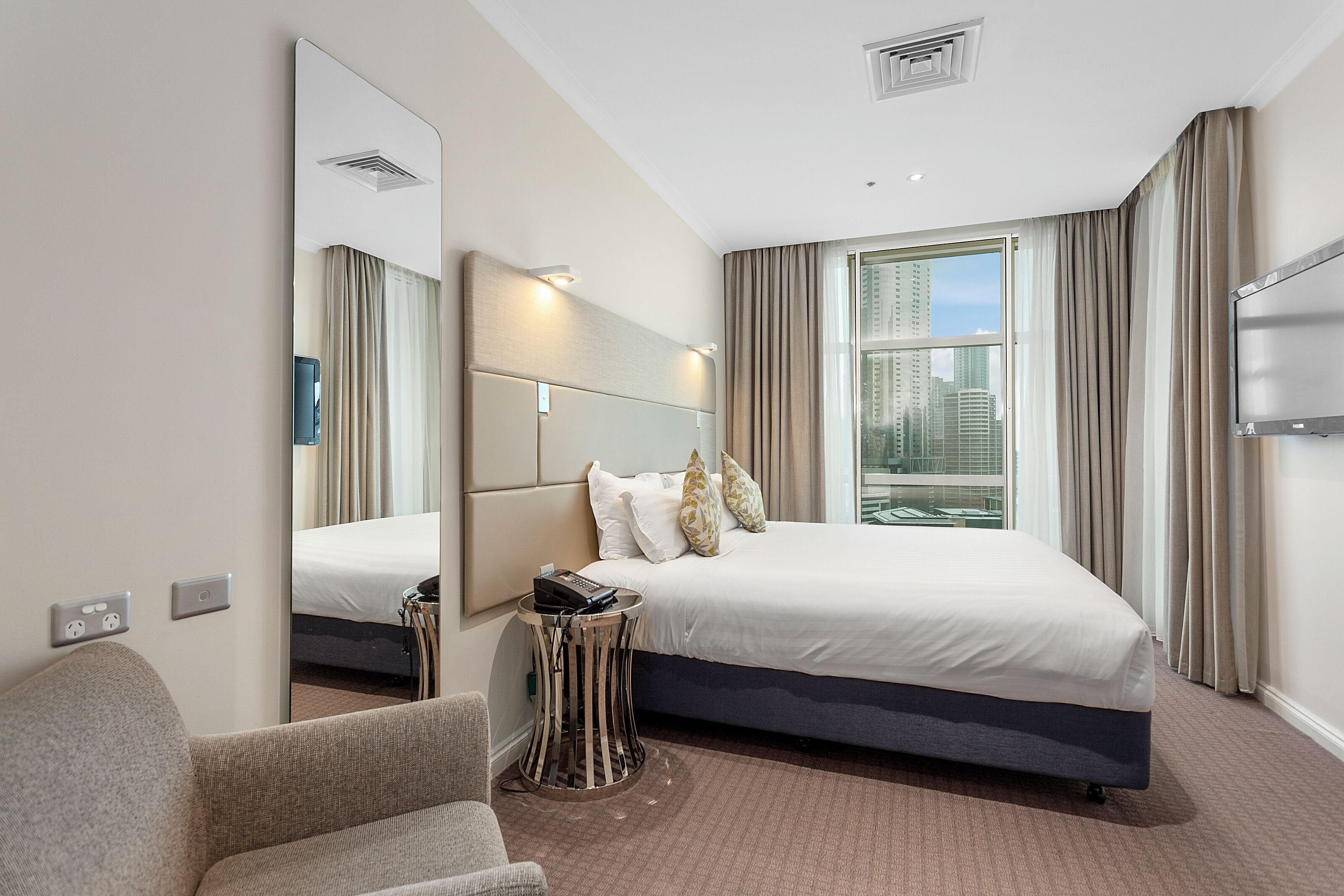 Habitación de hotel con una cama grande, un sofá, una mesita de noche con teléfono, un espejo y una ventana con cortinas.