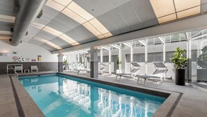 Une piscine intérieure à l’eau claire, entourée de chaises longues et de plantes en pot.