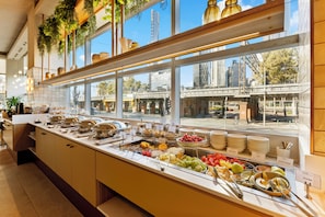 A buffet with a variety of food items and a view of the cityscape through large windows. - Clarion Suites Gateway (Melbourne)