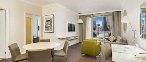 A hotel room with a round table, chairs, a sofa, a TV, a lamp, and a city view.