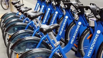 A row of blue bicycles with "Melbourne" branding, parked in a line on a sidewalk.
