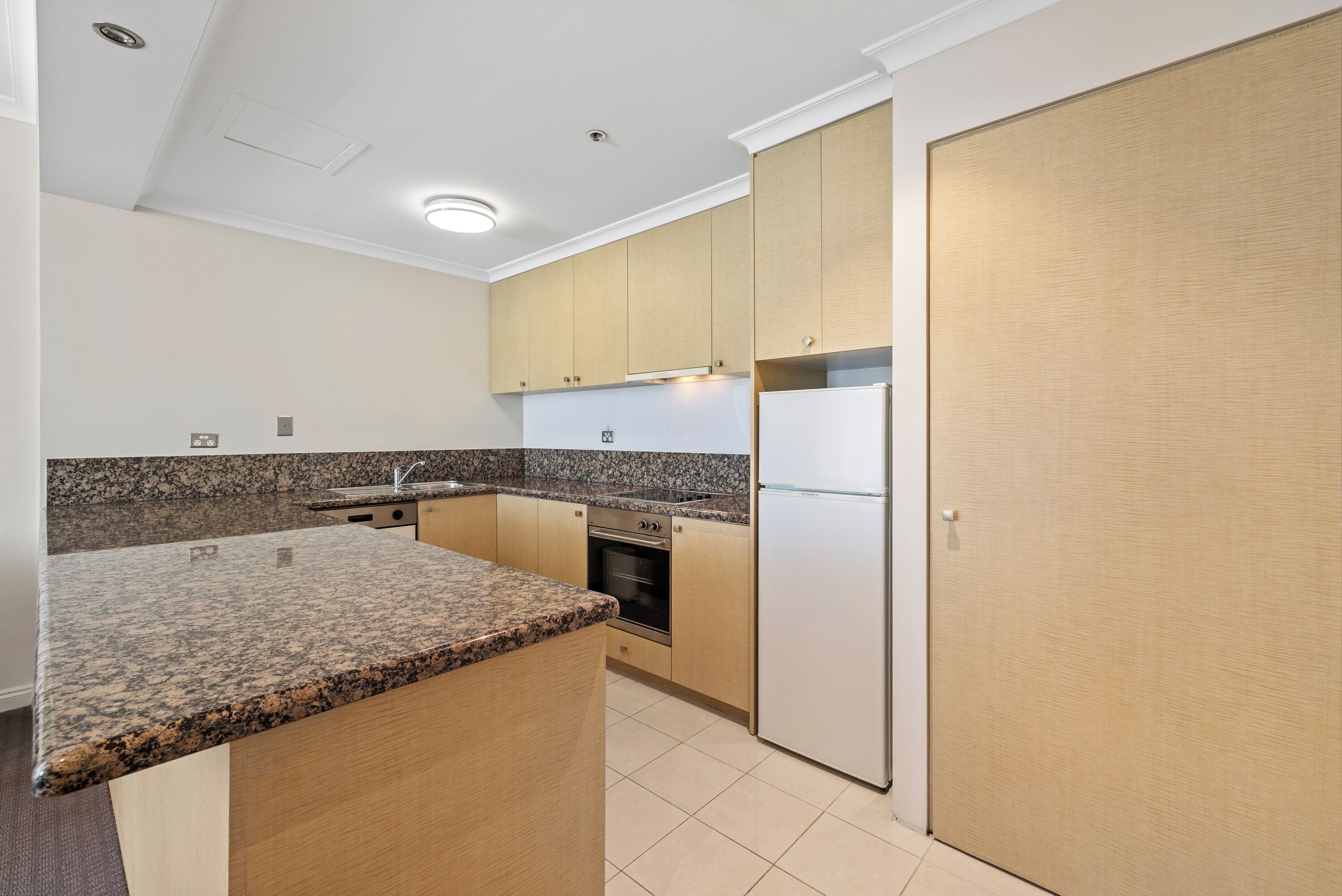 Eine Küche mit Granitarbeitsplatten, Holzschränken, einem eingebauten Ofen und einem Kühlschrank.