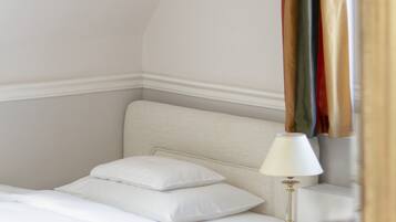 A bedroom with a bed, white bedding, a bedside lamp, and a mirror reflecting a colorful curtain.