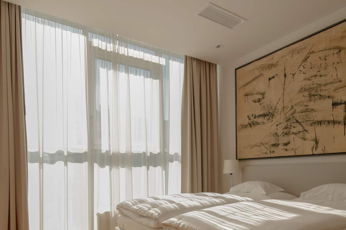 Ein Schlafzimmer mit einem großen Bett, einem Fenster mit durchsichtigen Vorhängen und einem Gemälde an der Wand.