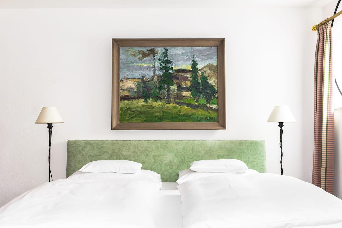 Ein Hotelzimmer mit einem Bett, zwei Nachttischlampen, einem gerahmten Bild an der Wand und einem grünen Kopfteil.
