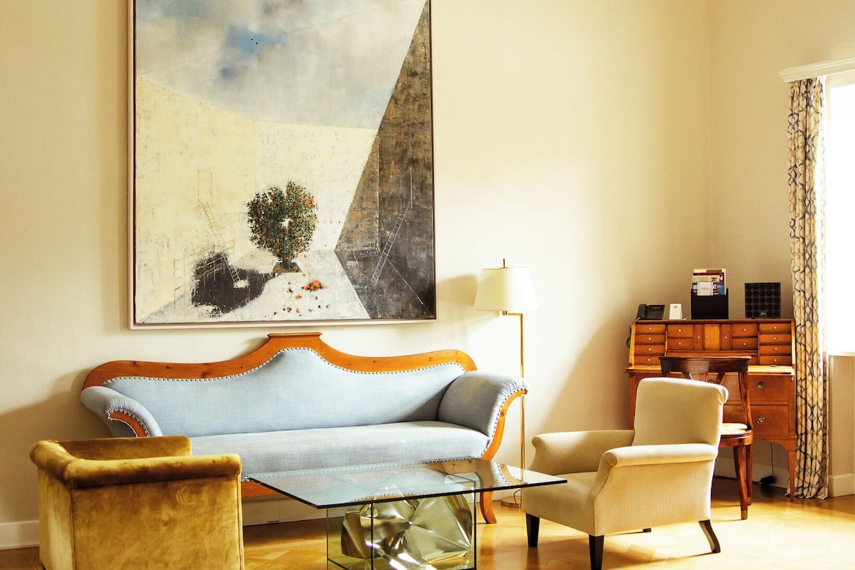 Ein Wohnzimmer mit einer Couch, Sesseln, einem Glastisch, einem Schreibtisch und einer Kristallleuchter.