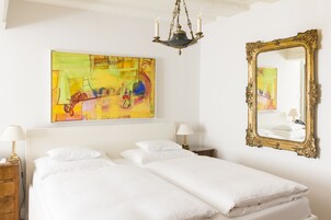 Habitación de hotel con una cama grande, una mesita de noche, una lámpara, un candelabro, un espejo y un cuadro abstracto de colores en la pared.