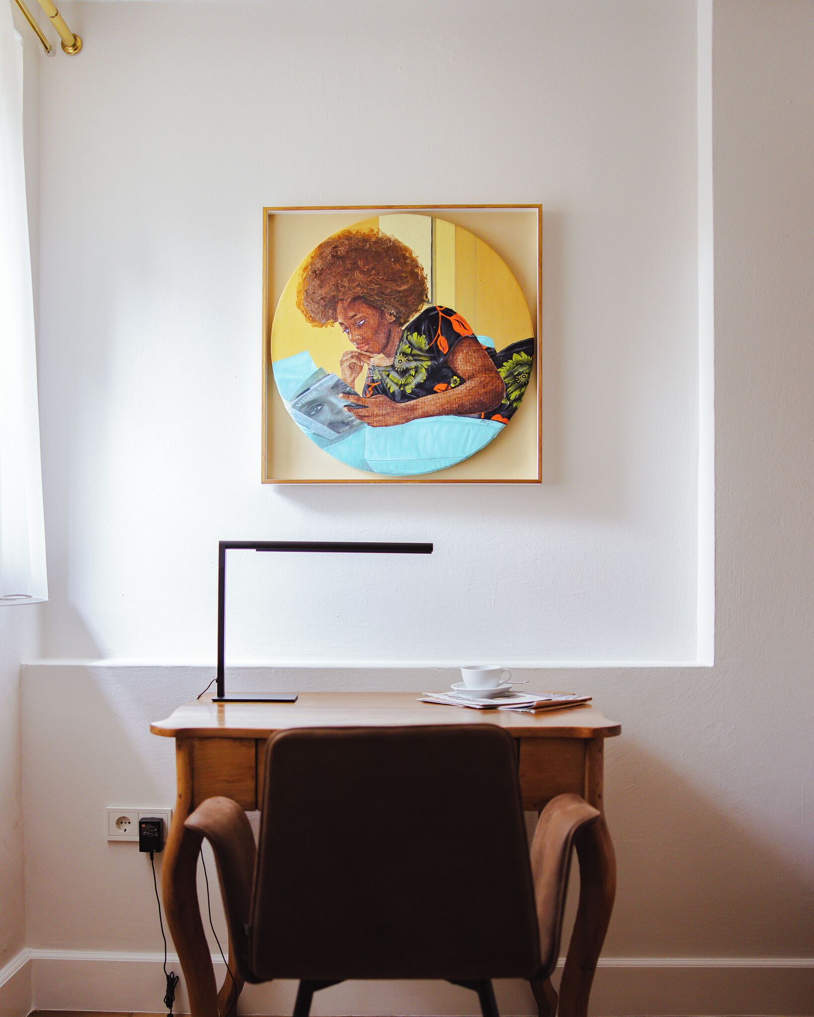 Ein Zimmer mit Schreibtisch, Stuhl und einem gerahmten Kunstwerk an der Wand.