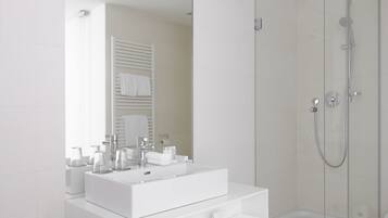 Ein modernes Badezimmer mit einem großen, weißen Waschbecken, einer Duschkabine aus Glas und einem Spiegel, der einen Handtuchhalter reflektiert.