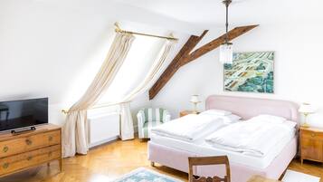Une chambre à coucher avec un lit, une télévision, une commode en bois, une chaise, une table et un tableau accroché au mur.