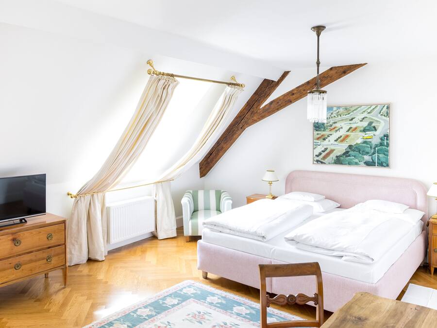 Une chambre à coucher avec un lit, une télévision, une commode en bois, une chaise, une table et un tableau accroché au mur.