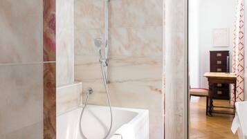 A bathroom with a bathtub, shower, and marble tiles.