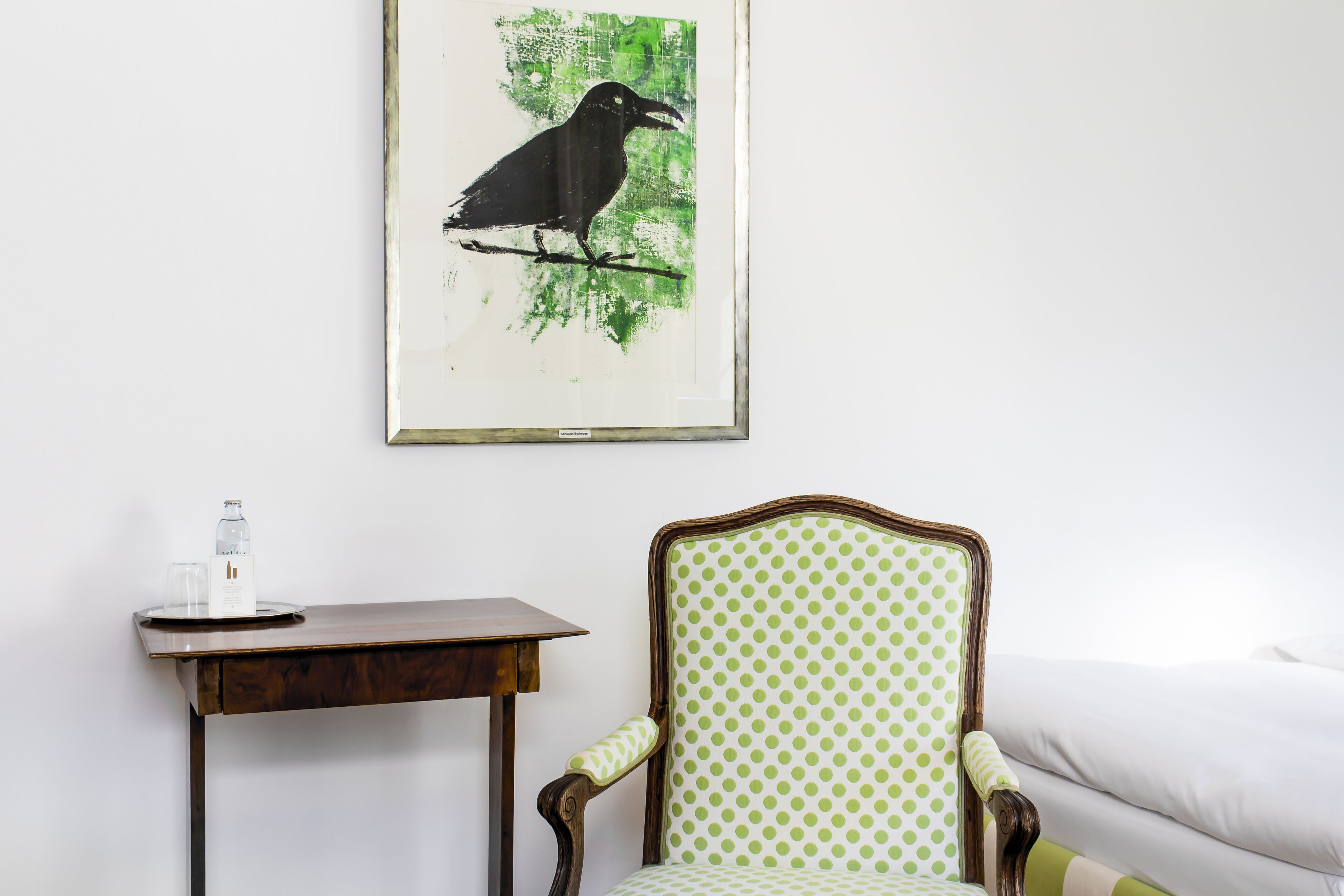 Ein Zimmer mit einem Holztisch, einem Stuhl mit grün gepunkteter Polsterung und einem Bilderrahmen mit einem Vogelbild an der Wand.