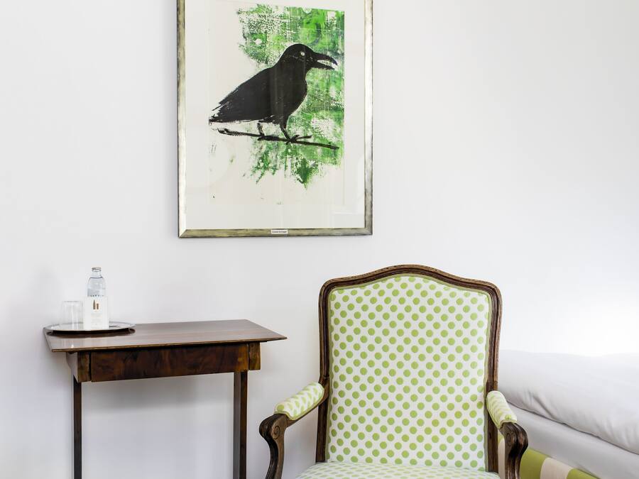 Ein Zimmer mit einem Holztisch, einem Stuhl mit grün gepunkteter Polsterung und einem Bilderrahmen mit einem Vogelbild an der Wand.