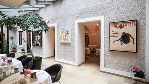 A modern dining area with round tables, black chairs, and a large tree providing shade. - Schlossberghotel (Graz)