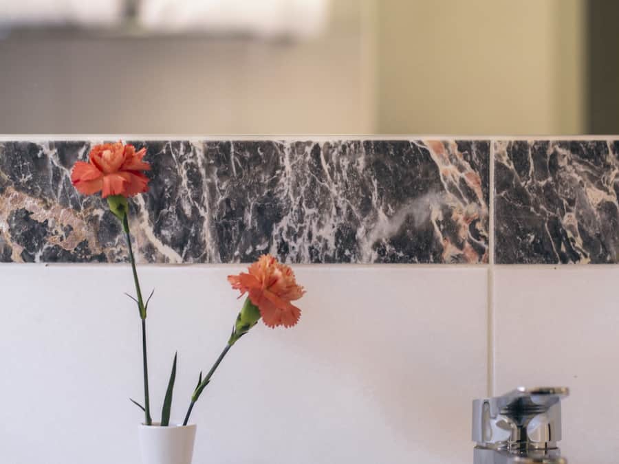 A bathroom with a white marble sink, a white vase with orange flowers, and a chrome faucet.