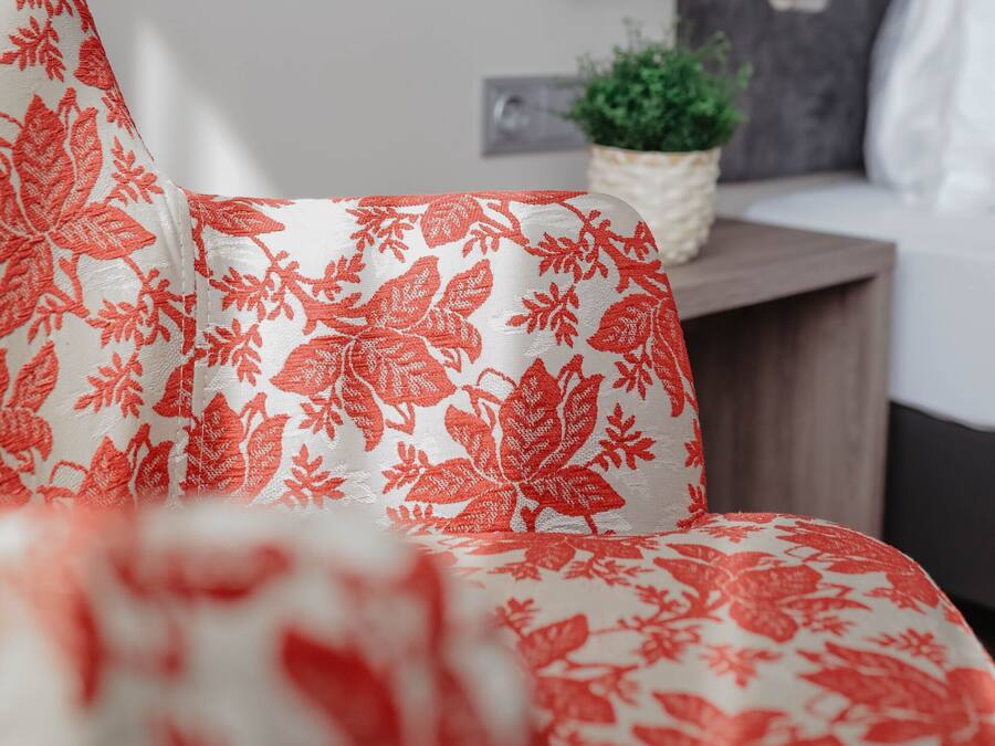 A bed with red floral bedding, a bedside lamp, a small potted plant, and a headboard.