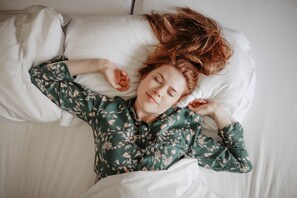 A person lying in bed with a floral-patterned shirt, white bedding, and a pillow.