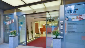 A hotel entrance with glass doors, a red carpet, and a signboard with hotel names and amenities. - Stadtoase Kolping Hotel (Linz)