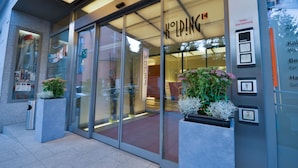 A hotel entrance with glass doors, a sign reading "KÖLPING," and a small outdoor planter with flowers. - Stadtoase Kolping Hotel (Linz)