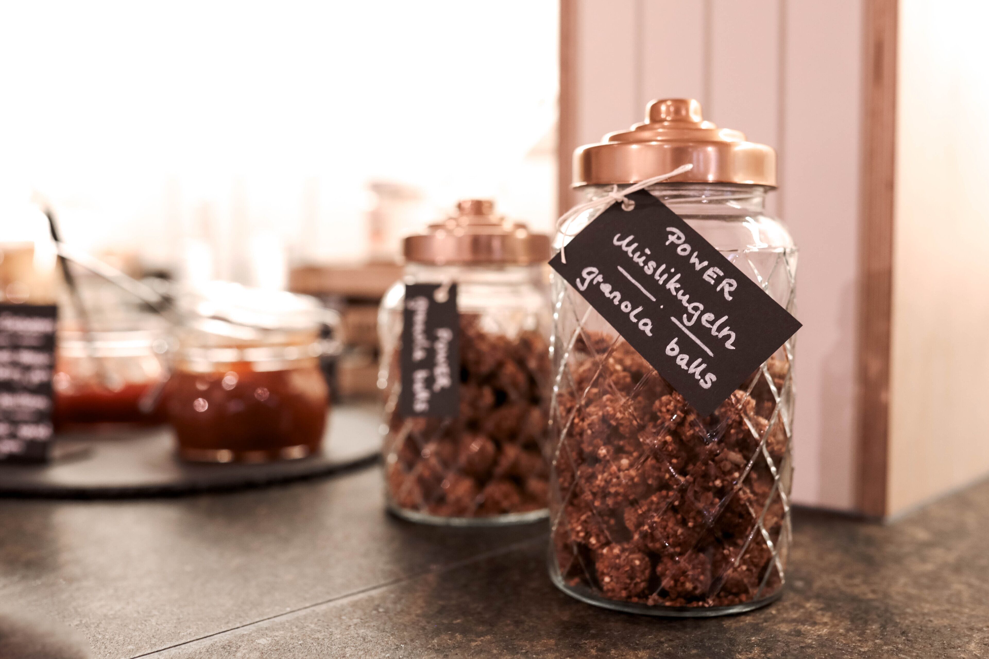 A display of granola balls in glass jars with labels, arranged on a countertop.