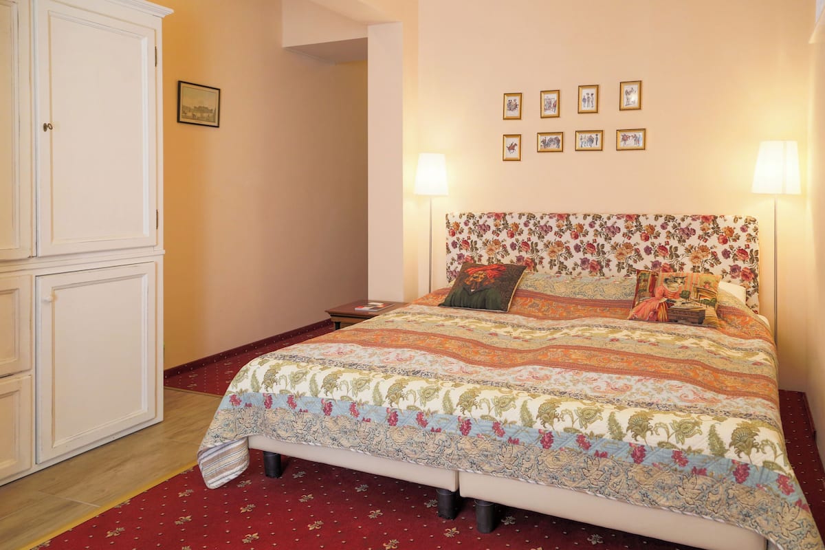 A bedroom with a floral-patterned bedspread, a white wardrobe, and a red carpet.