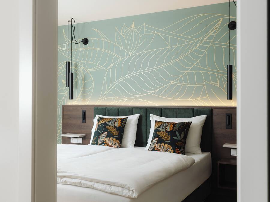 Un dormitorio moderno con una cama, dos almohadas decorativas, una lámpara de pared y una mesita de noche.