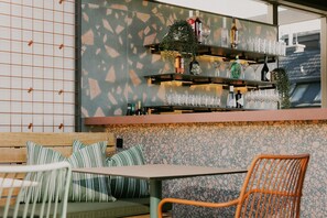 An outdoor seating area with a bar counter, cushioned seating, and a patterned wall.