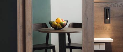 Un coin repas avec une table ronde, des chaises et un saladier rempli de fruits.
