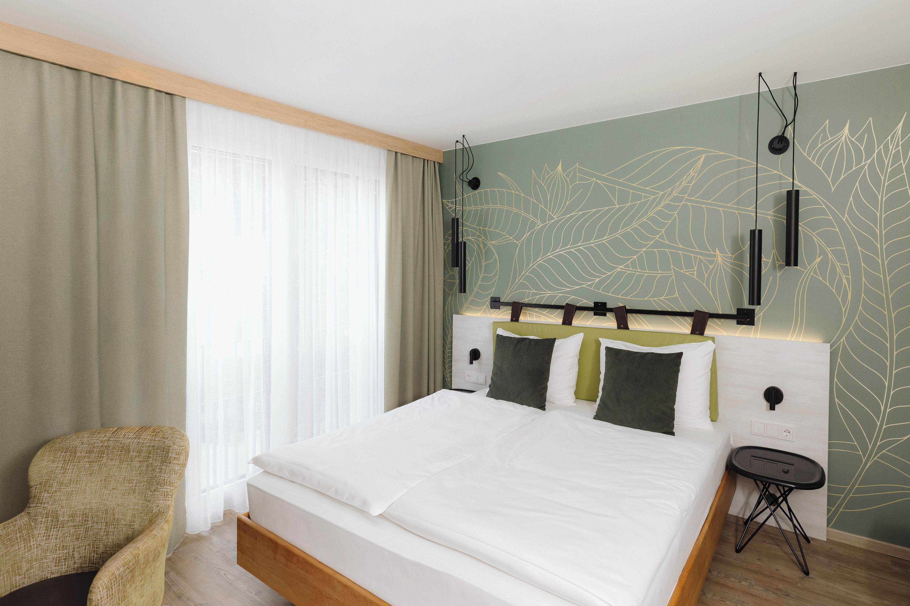 Une chambre d’hôtel avec un lit, une chaise, une table de chevet et un mur orné d’un motif de feuilles.