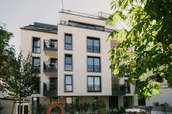 A multi-story building with balconies, a rooftop terrace, and a garden area with outdoor seating.