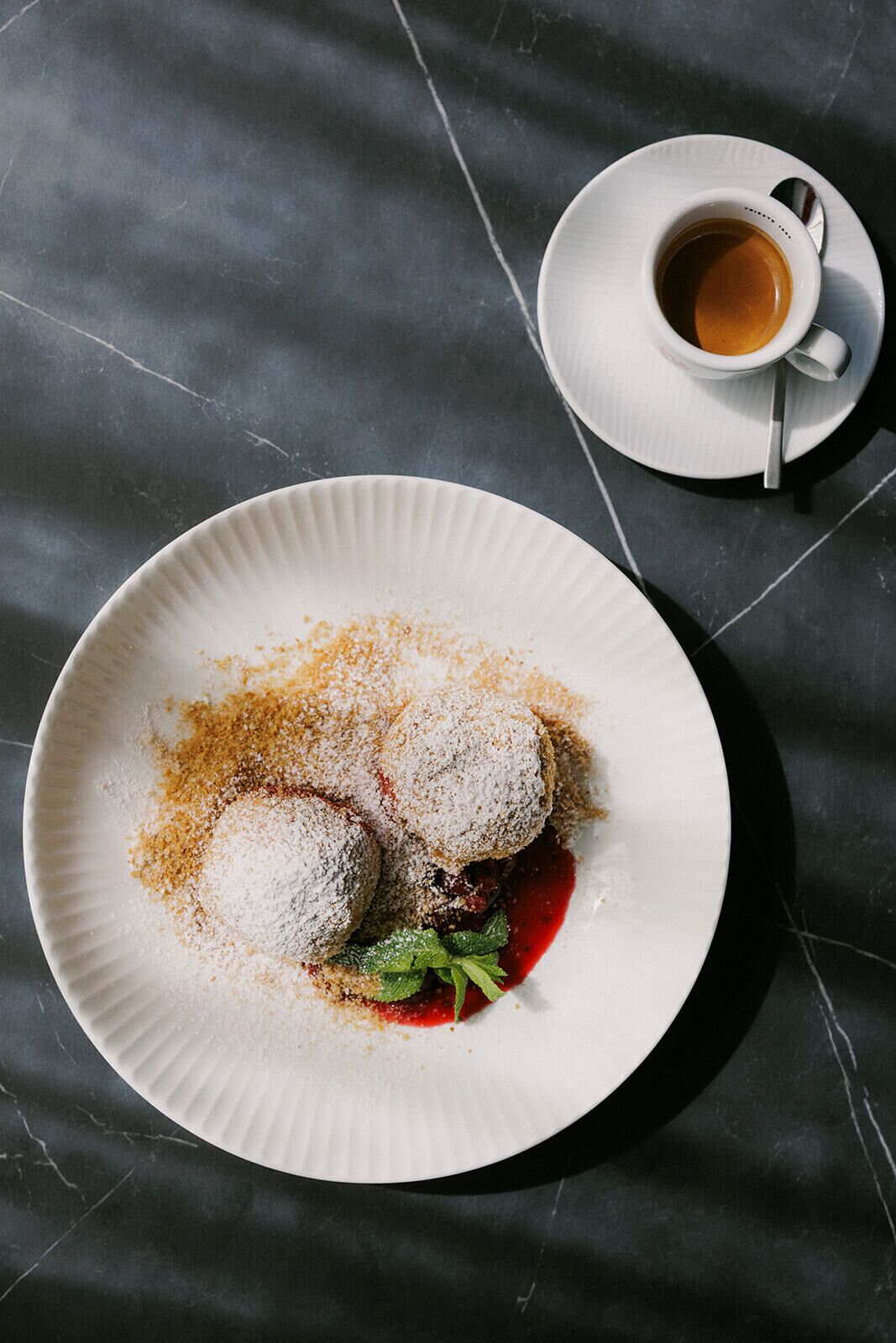 A plate with two dumplings, a sprig of mint, and a red sauce on a dark marble surface.