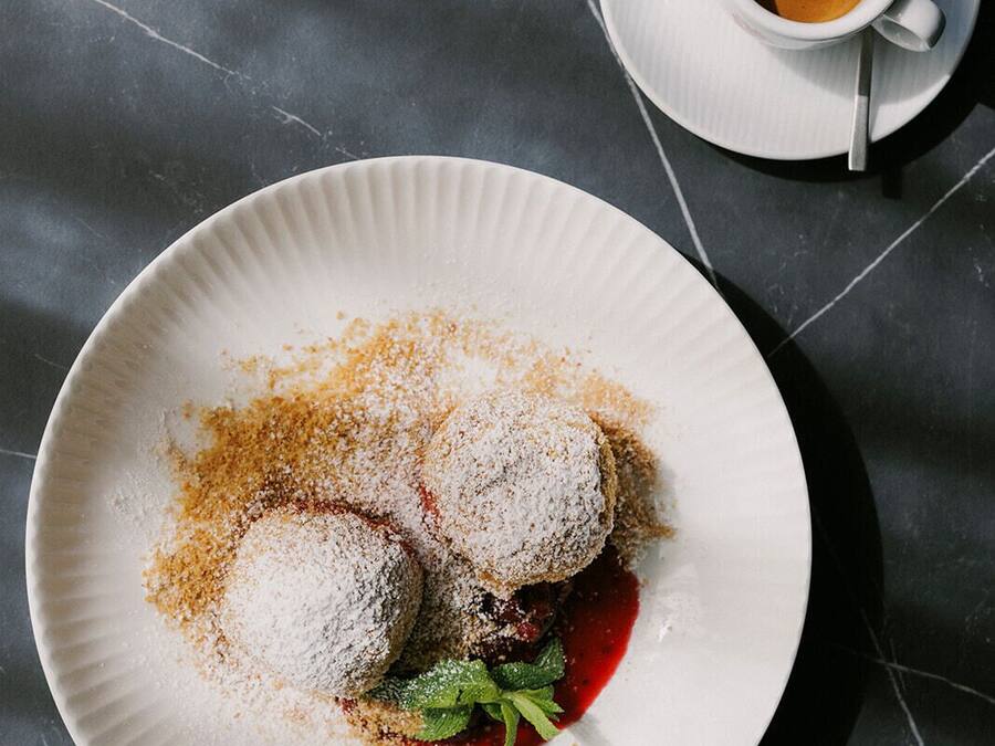 A plate with two dumplings, a sprig of mint, and a red sauce on a dark marble surface.