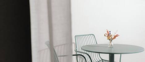 Una mesa de vidrio redonda con un florero, dos sillas de malla verde y una pared blanca.